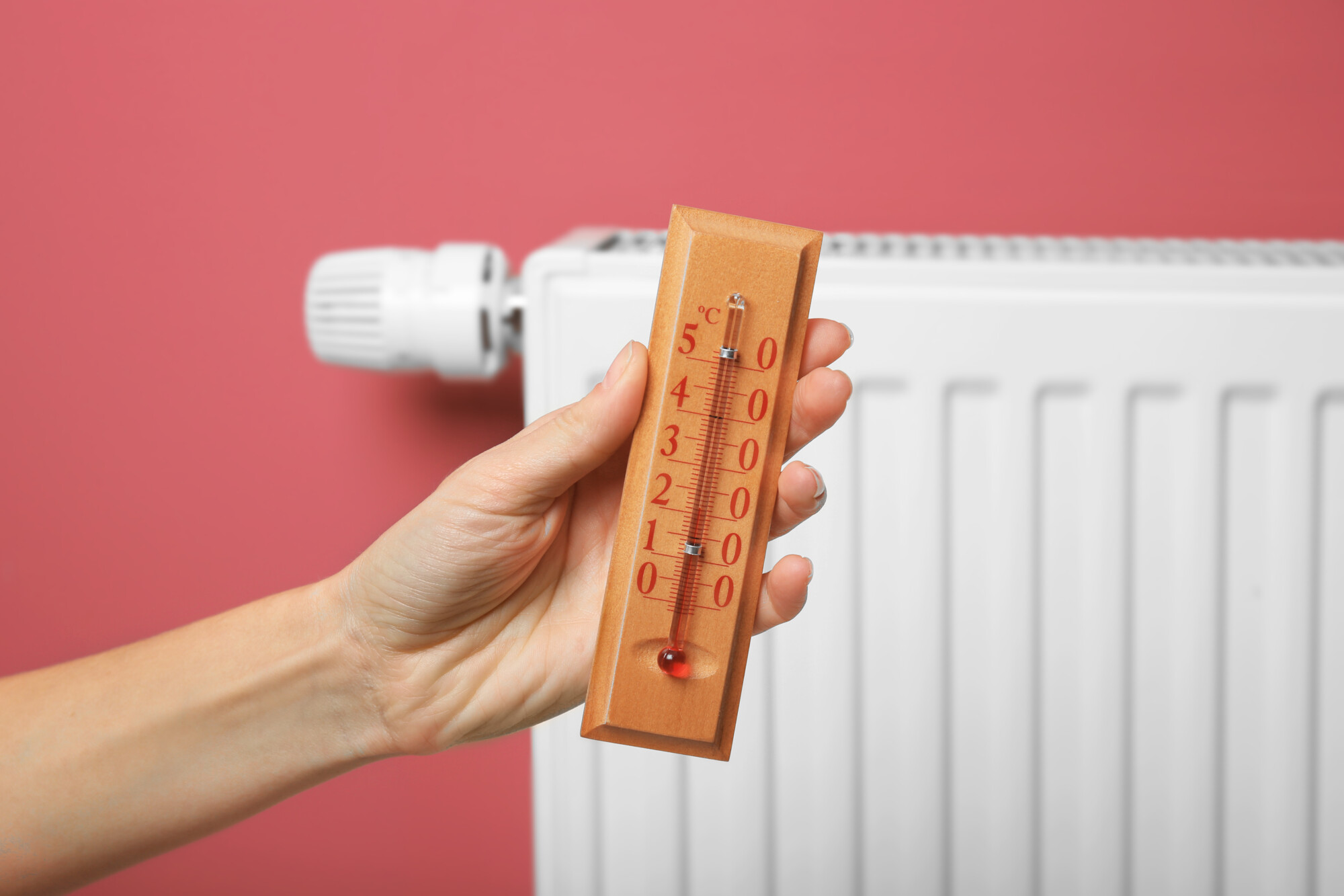 Female hand holding thermometer near heating battery tipi di riscaldamento