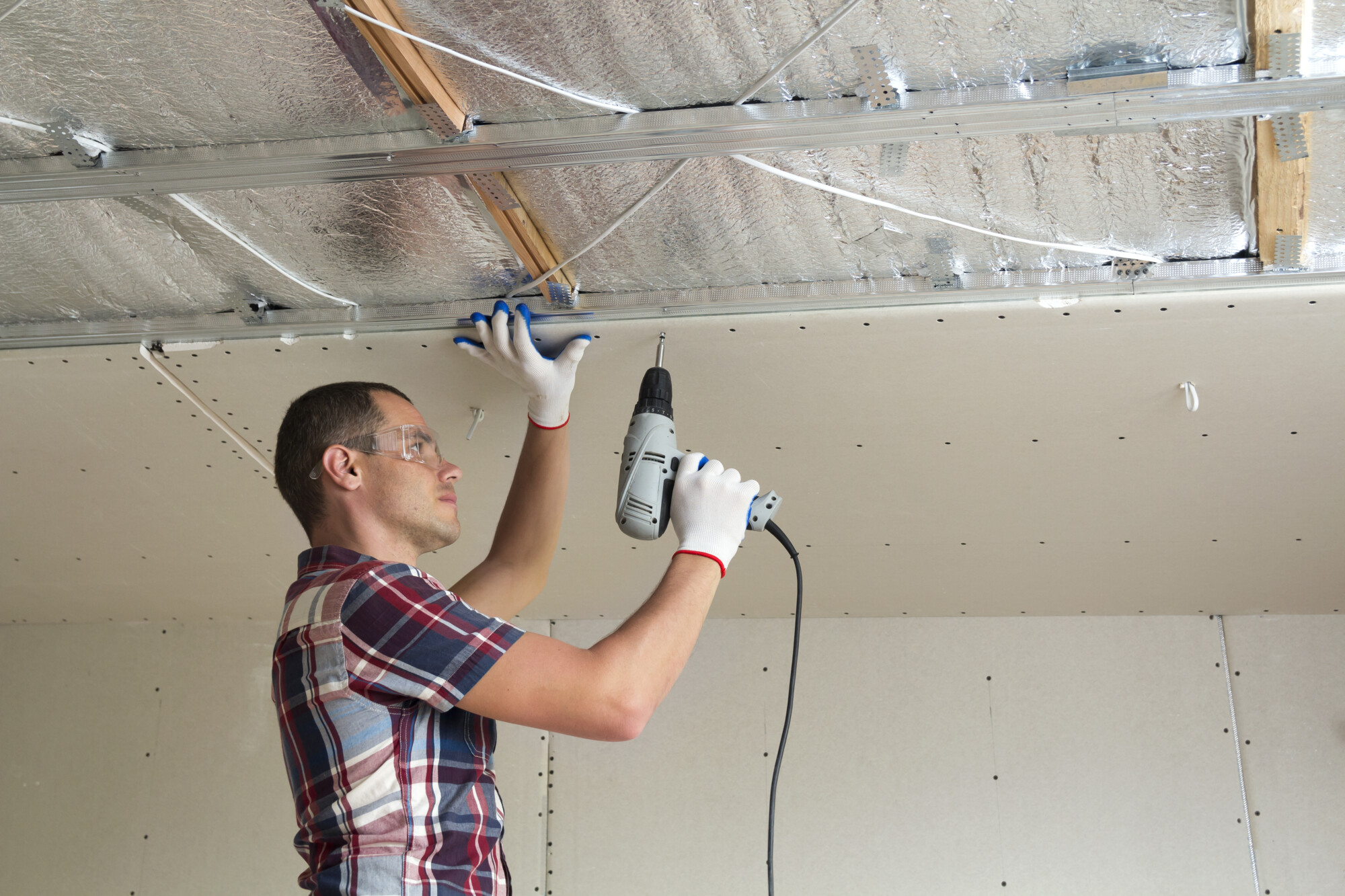 Young man in goggles fixing drywall suspended ceiling to metal f soffitto radiante